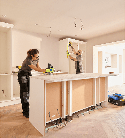 Two workers installing a kitchen cabinet.